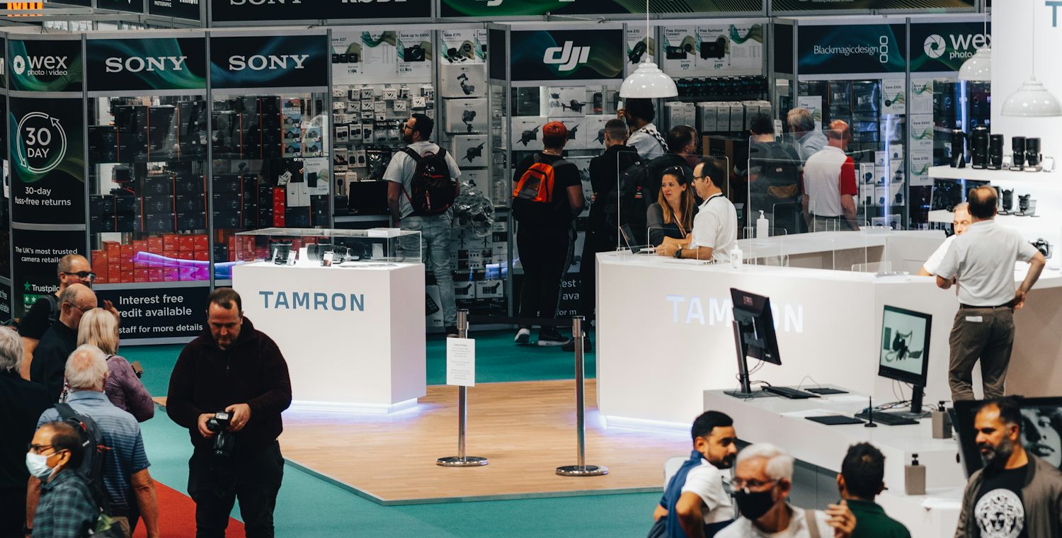 A crowded trade show aisle: visitors walking past a row of exhibitor stands