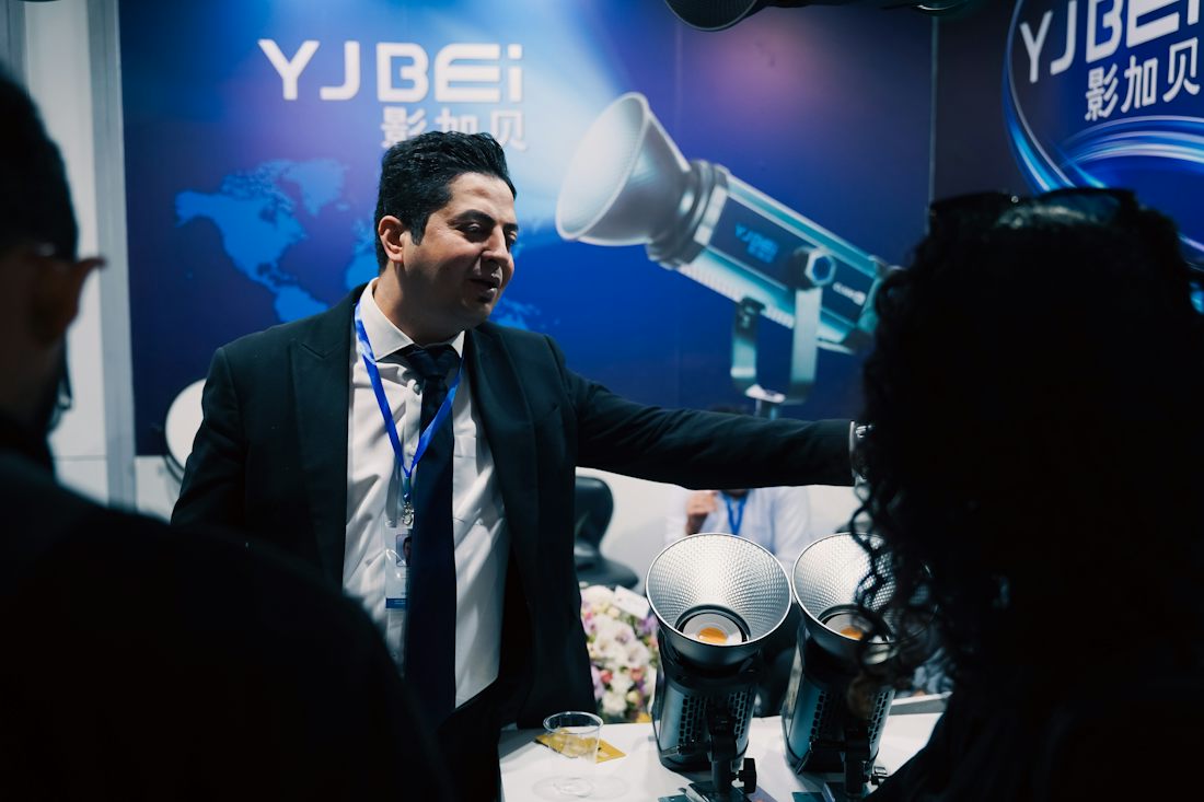 An exhibitor in a suit demonstrating a piece of equipment to visitors at the stand